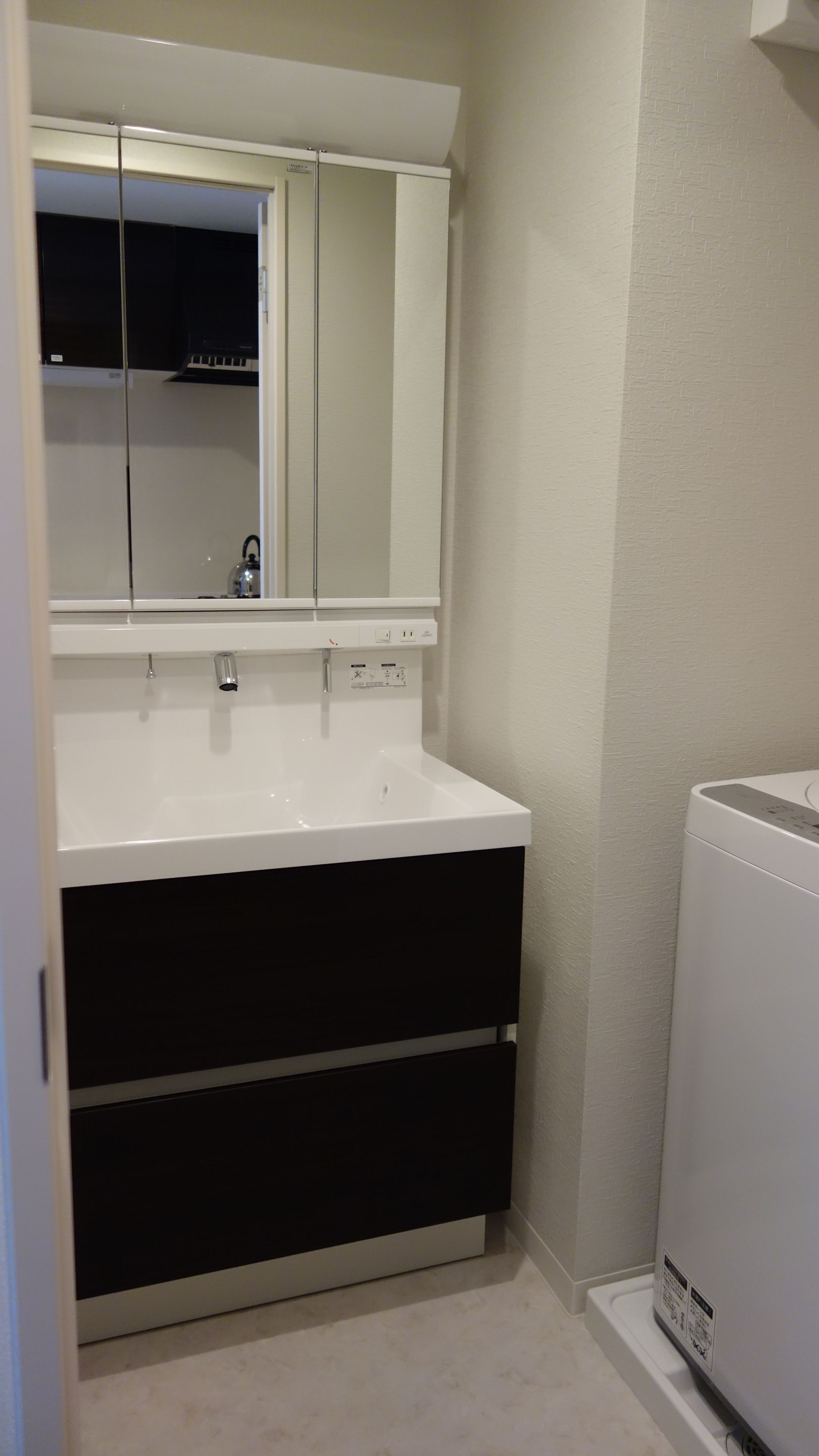 A bathroom with a white sink, black cabinets, and a white washing machine.