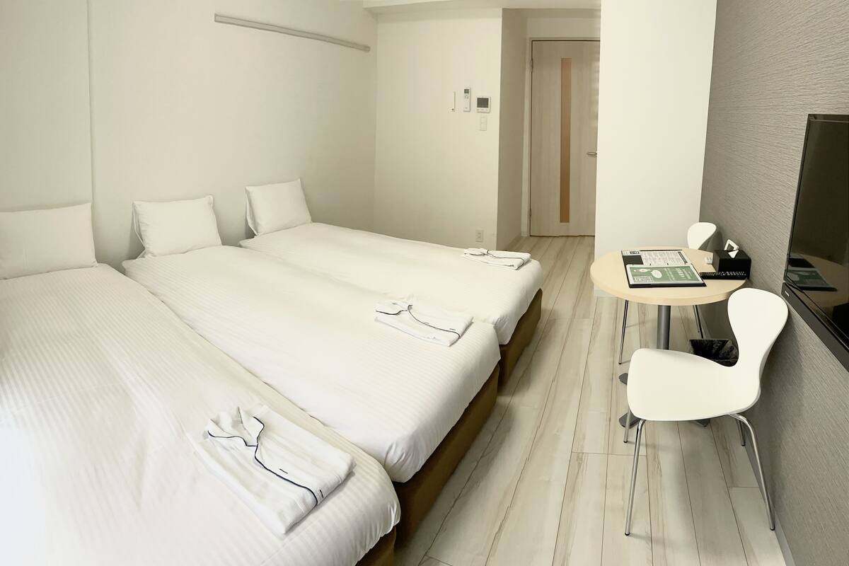 A hotel room with two beds, a small desk with a chair, a television, and a door leading to another room.