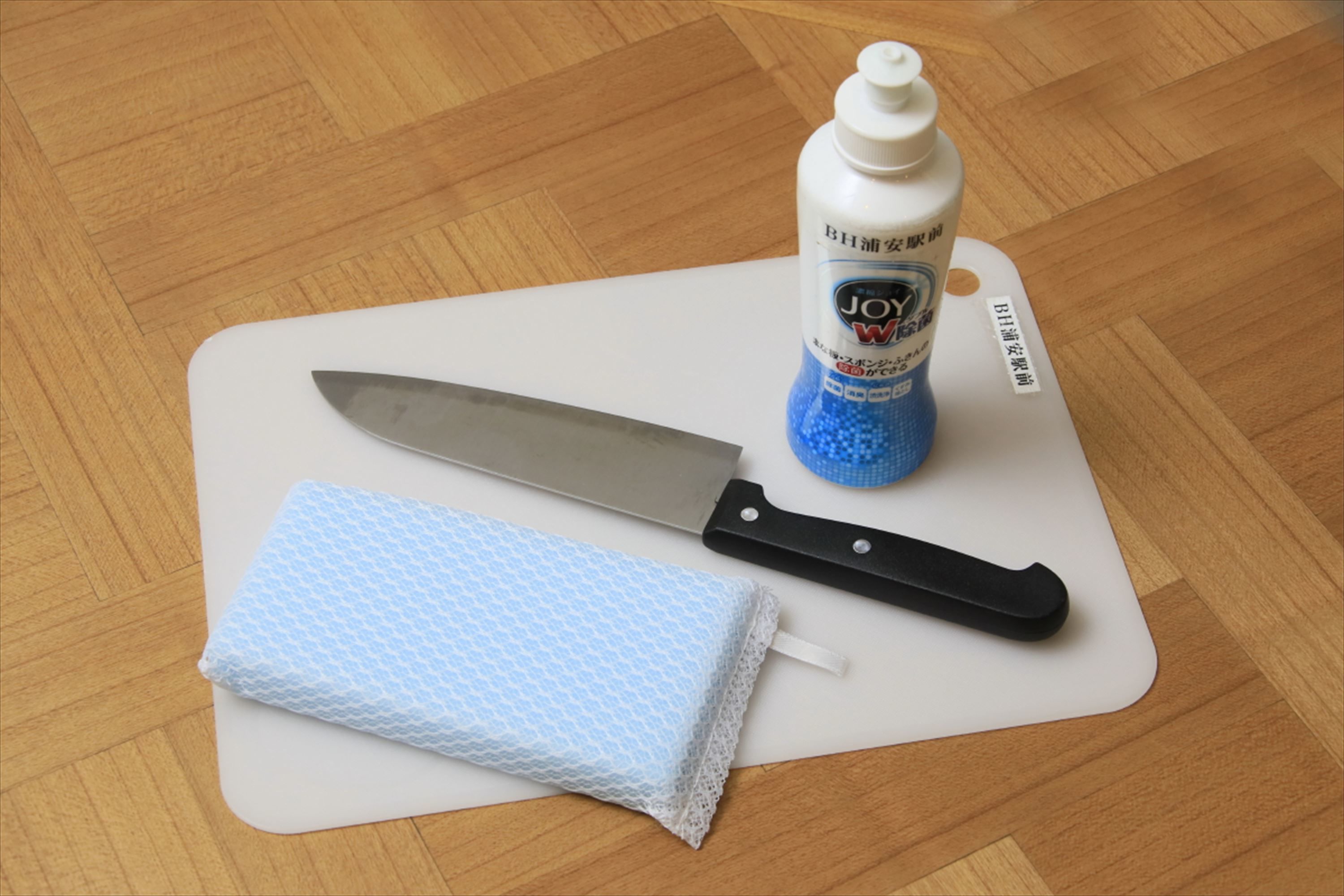 Una tabla de cortar, un cuchillo y una botella de solución limpiadora sobre un piso de madera.