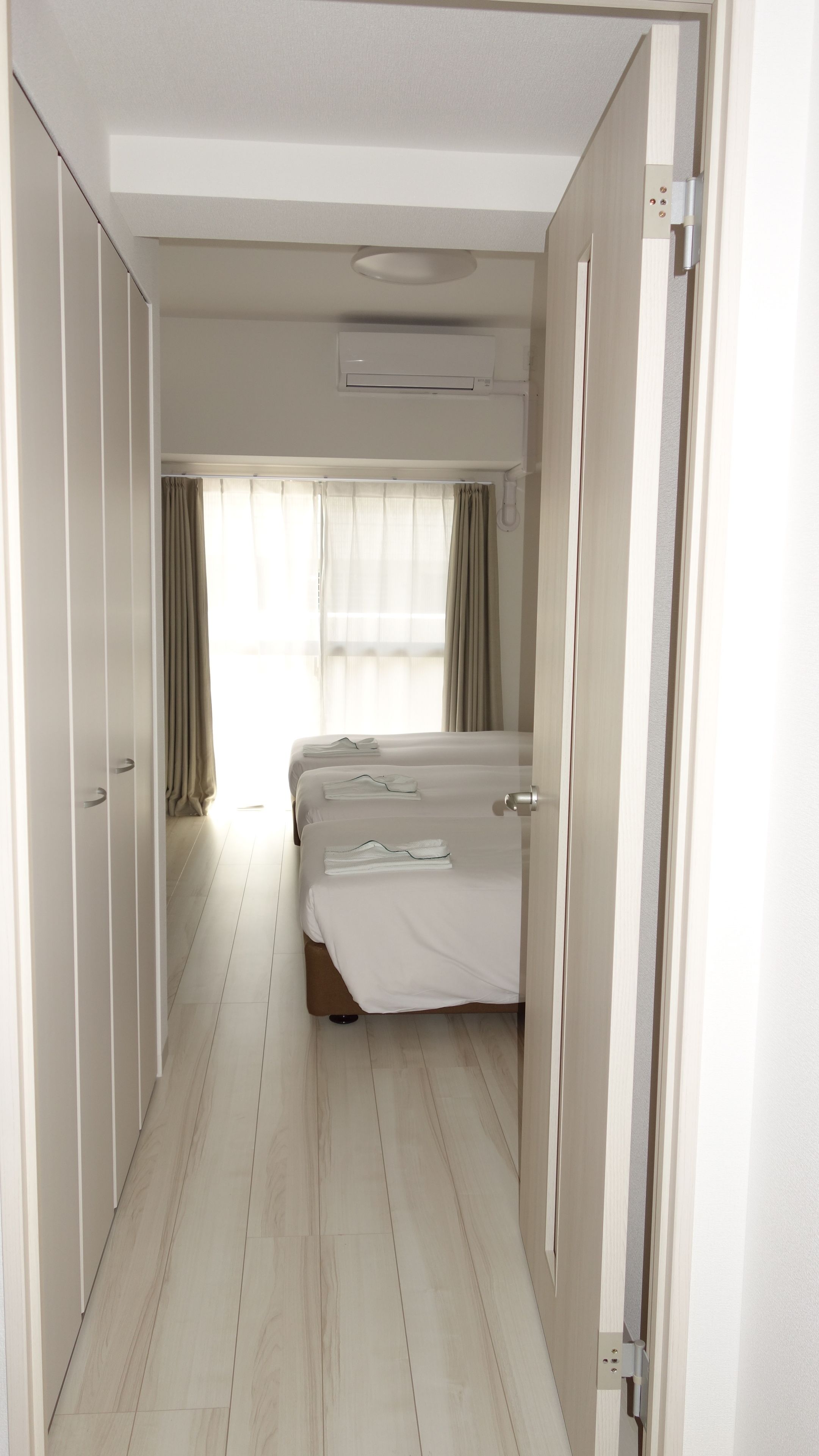 A hotel room with a central bed, two side beds, a wardrobe, and an air conditioning unit.