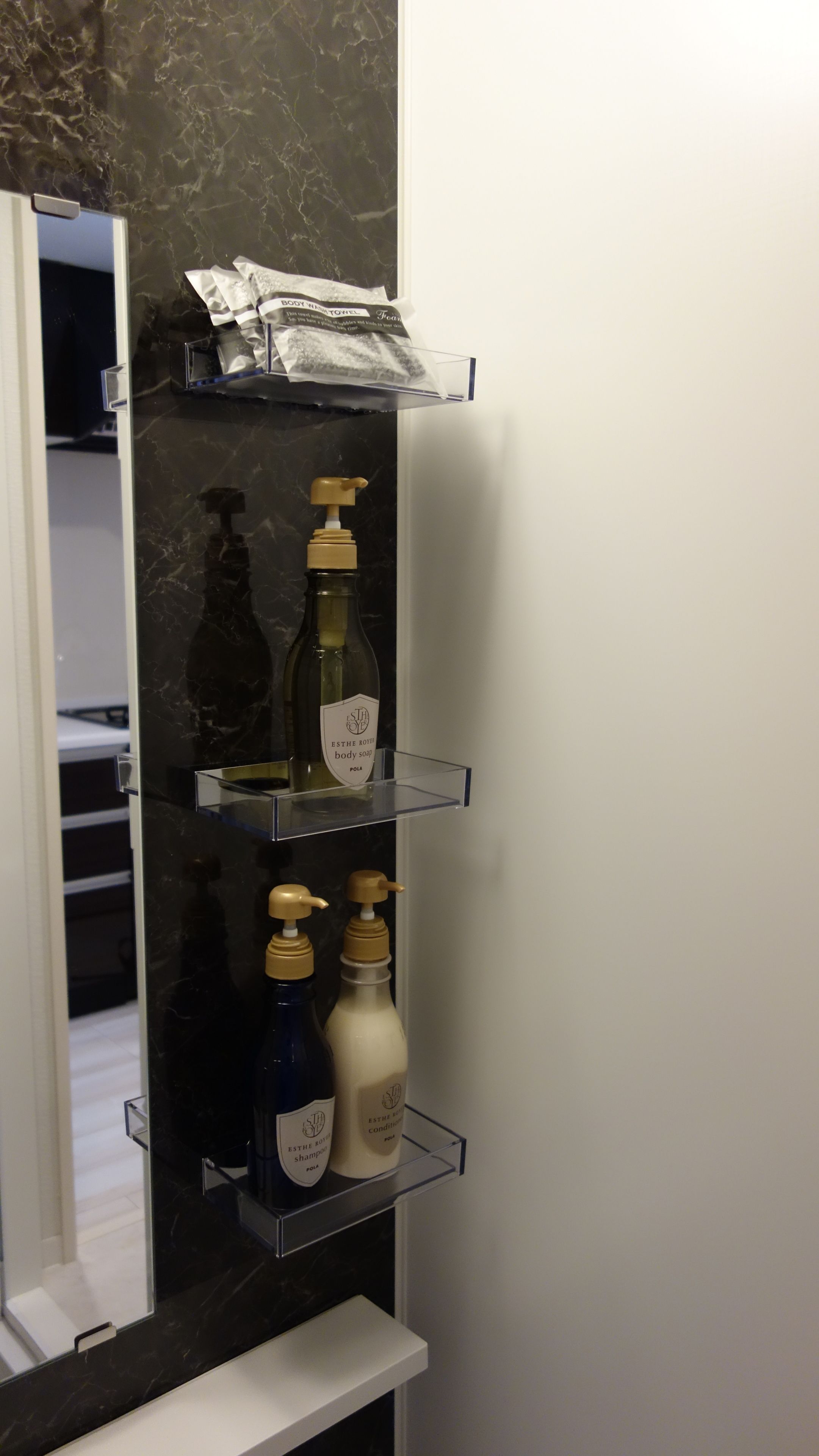 A bathroom with a black marble countertop, a mirror, and shelves holding toiletries including body soap, shampoo, and conditioner.