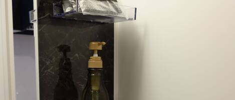 A bathroom with a black marble countertop, a mirror, and shelves holding toiletries including body soap, shampoo, and conditioner.