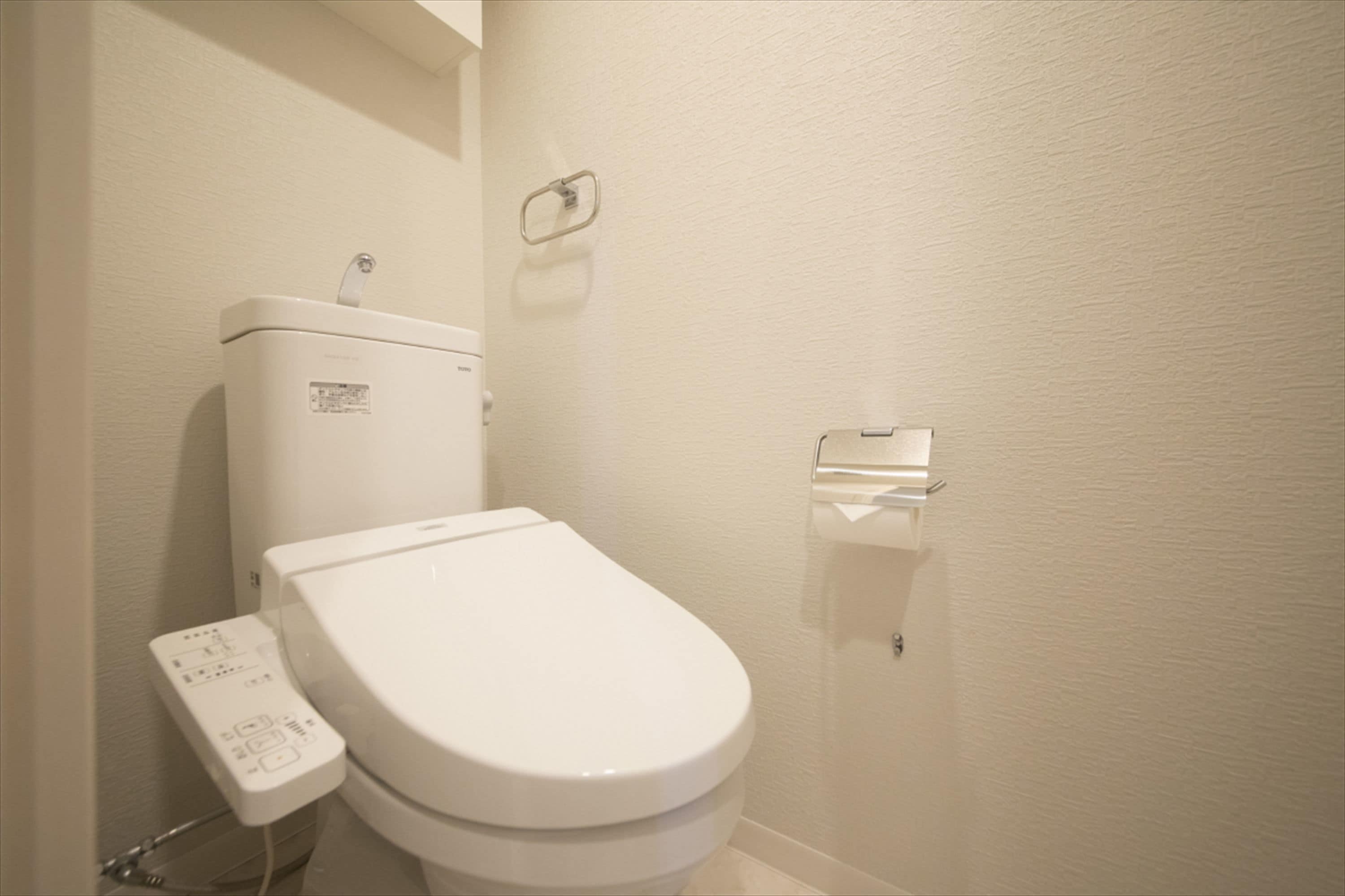 Inodoro blanco con panel de control y dispensador de toallas de papel montado en la pared.