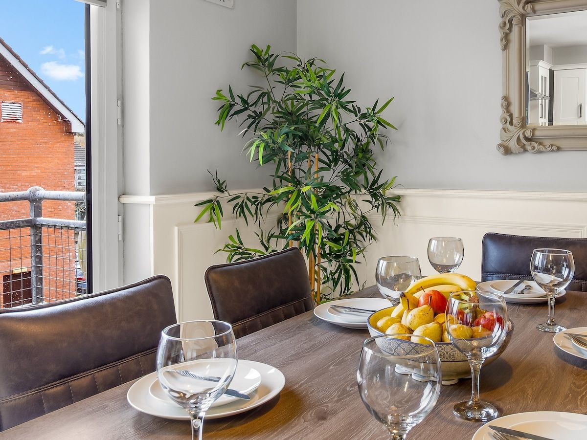 A dining area with a table set for four, a potted plant, and a view of a brick building outside.