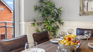 A dining area with a table set for four, a potted plant, and a view of a brick building outside.