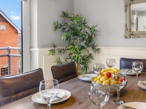 Un coin repas avec une table dressée pour quatre personnes, une plante en pot et une vue sur un bâtiment en briques à l’extérieur.