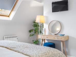 Une chambre à coucher avec un lit, une table de chevet avec une lampe, un miroir et un téléviseur fixé au mur.