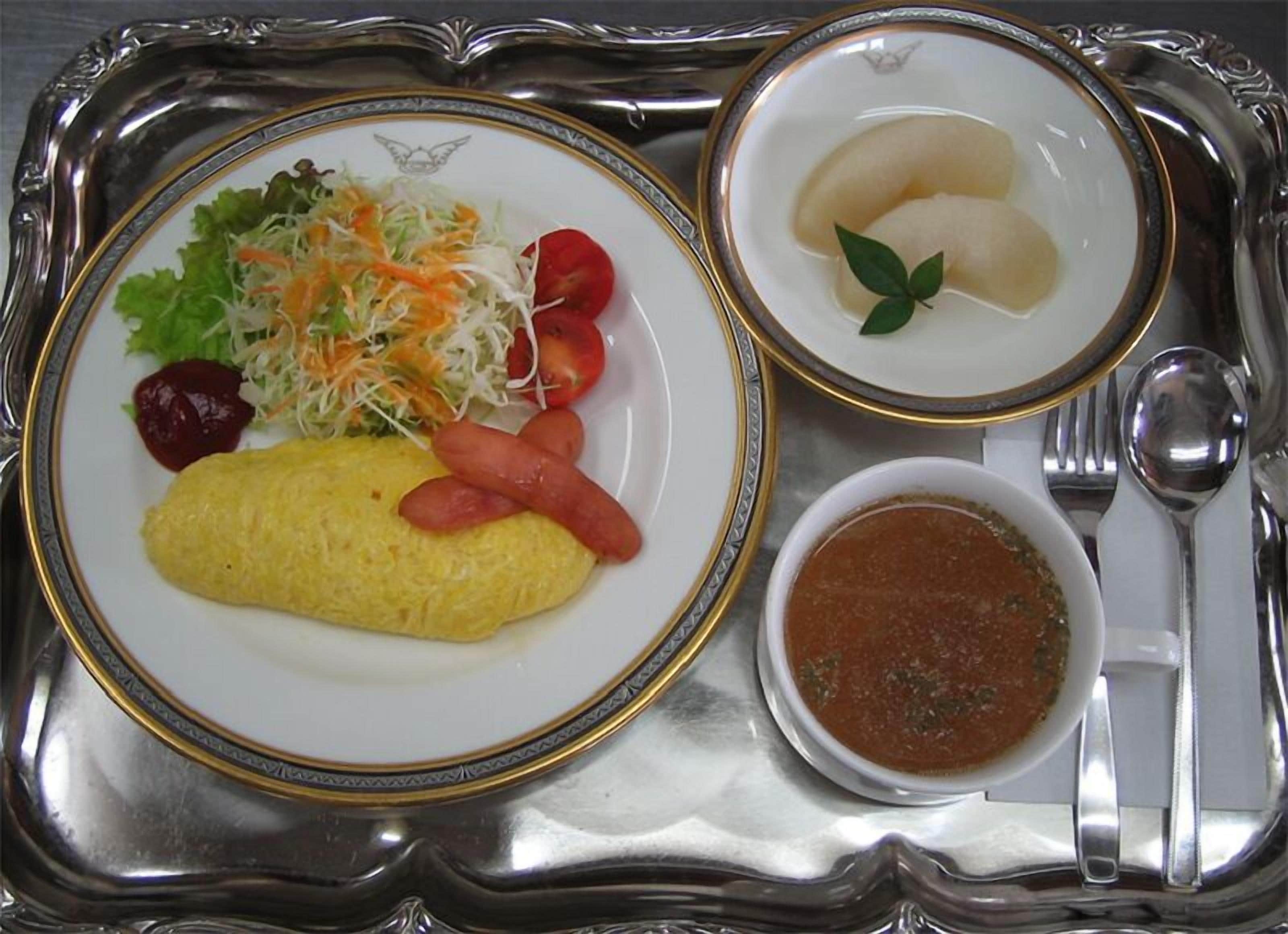A tray with a plate of food including an omelet, vegetables, and sausages, a bowl of soup, and a small dish with dumplings.