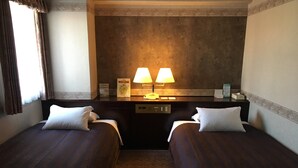 Ein Hotelzimmer mit zwei Einzelbetten, einem Nachttisch mit Lampe, einem Spiegel und einem kleinen Tisch mit Telefon und Taschentuchbox.