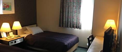 Quarto de hotel com duas camas de solteiro, uma escrivaninha com abajur, telefone e televisão.