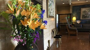 Eine Lobby mit einer großen Blumenvase, einem Empfangstresen, einer Sitzecke mit einer Couch und Sesseln sowie einem gerahmten Kunstwerk an der Wand.