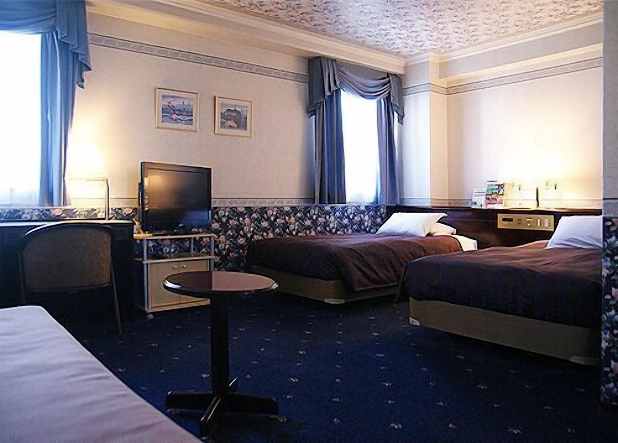 A hotel room with two beds, a TV, a desk, and a small round table.