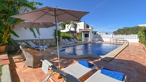 A poolside area with lounge chairs, a large umbrella, and a stone wall. - Classic and comfortable villa in Javea, on the Costa Blanca, Spain  with private pool for 6 persons (Javea)