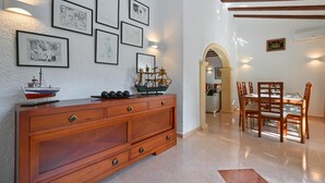 A dining area with a wooden table and chairs, a wooden cabinet with artwork, and a hallway with an archway. - Classic and comfortable villa in Javea, on the Costa Blanca, Spain  with private pool for 6 persons (Javea)