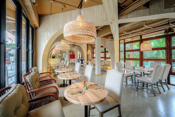 A restaurant with round tables, wicker chairs, and hanging lamps.