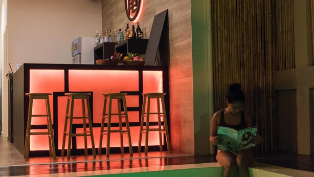 Een bar met krukken en een aanrecht, een persoon die een tijdschrift leest, en een groen verlichte muur.