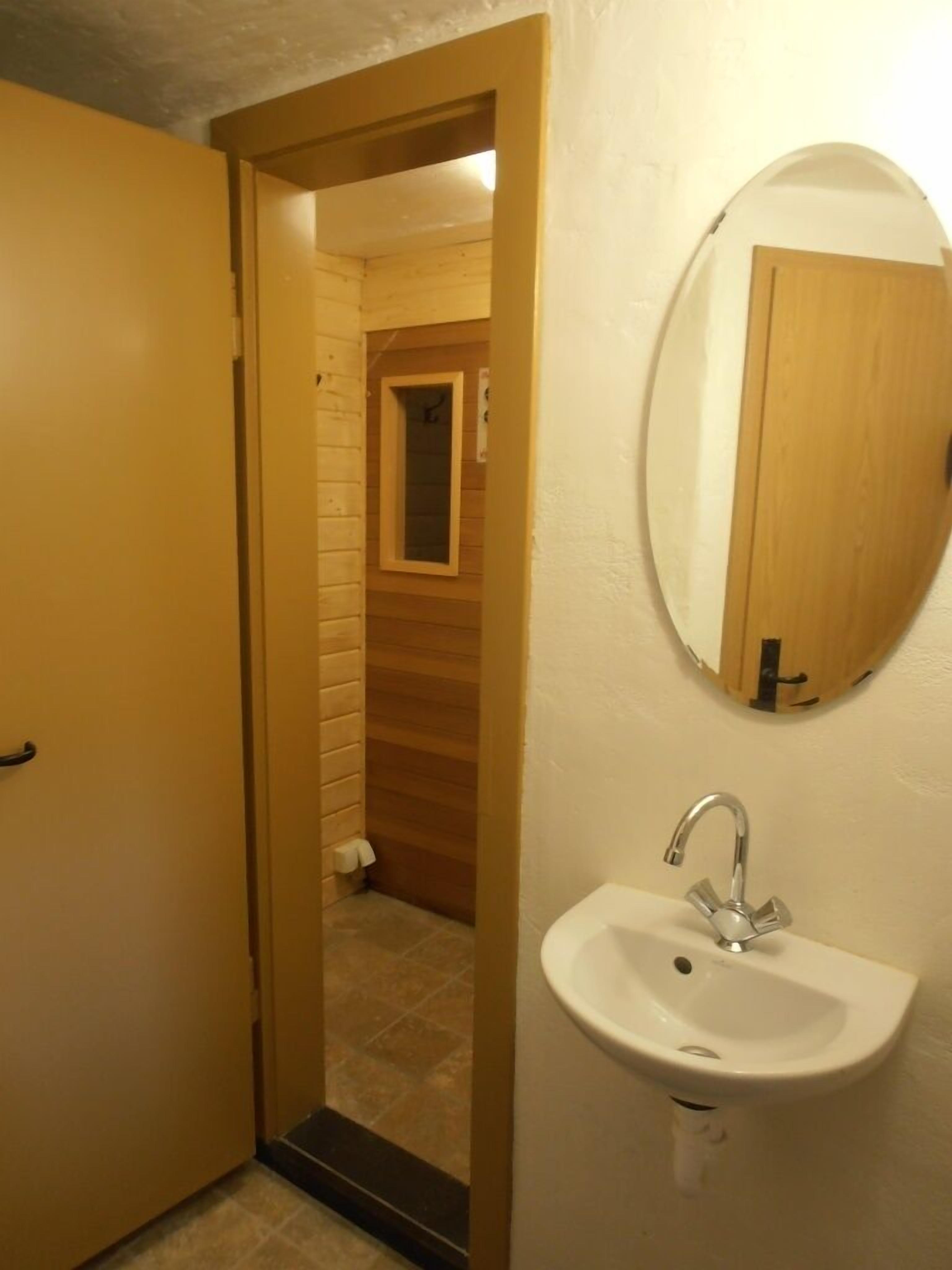 Une salle de bain avec une porte en bois, un lavabo avec un miroir et un sol carrelé.