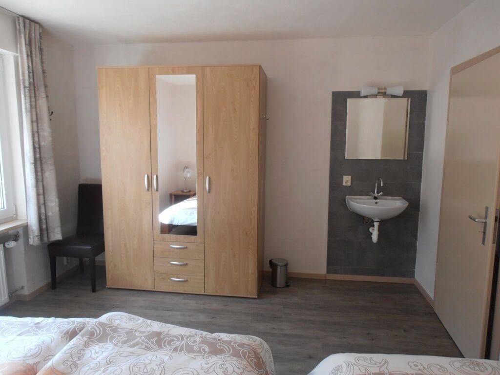 Een hotelkamer met een kledingkast, een bed, een klein bureau en een badkamer met een wastafel en spiegel.