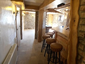 A narrow hallway with a stone wall, wooden beams, and a bar area with stools.