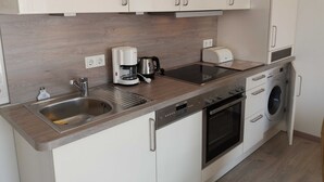 Eine kompakte Küche mit Einbauherd, Kaffeemaschine, Toaster und Waschmaschine.