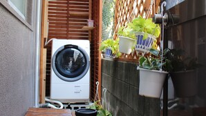 Un espacio exterior reducido con lavadora, mesa de madera y plantas colgantes en macetas.