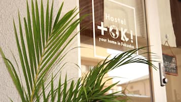 En skylt med texten ”Hostel Toki” sitter på fasaden av en byggnad, och i förgrunden står en krukväxt.