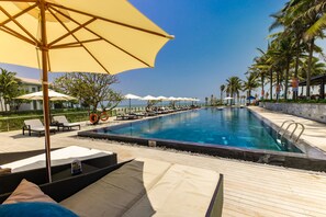 A poolside area with lounge chairs, umbrellas, and a clear view of the ocean.