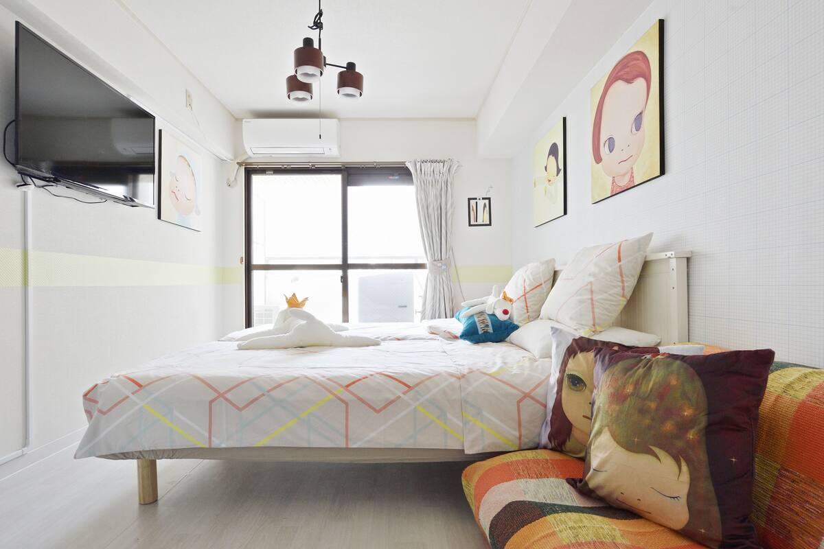 Une chambre à coucher avec un lit, une fenêtre avec des rideaux, un téléviseur fixé au mur et un luminaire au plafond.