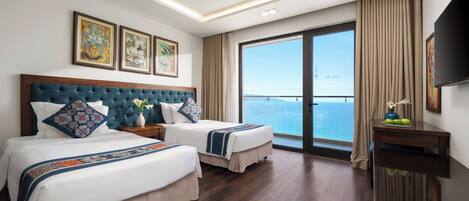 Une chambre d’hôtel avec deux lits, une grande fenêtre donnant sur la mer et des œuvres d’art accrochées au mur.