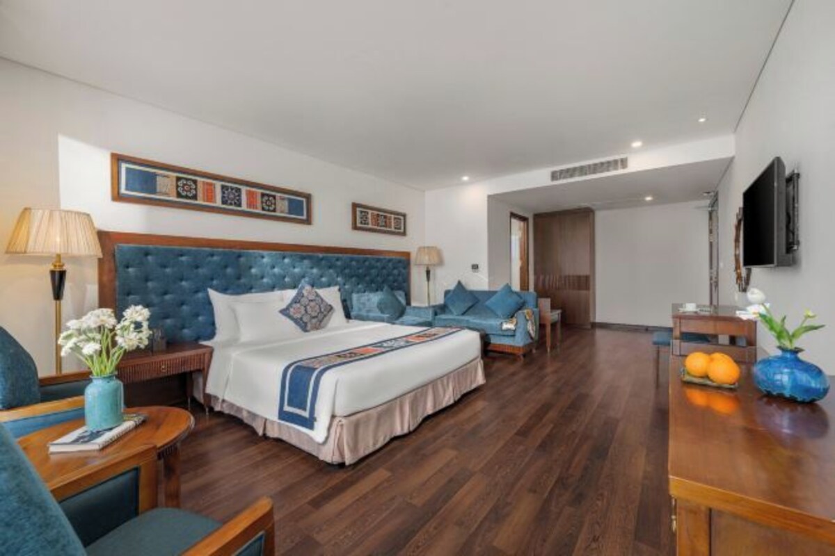 A hotel room with a large bed, a sofa, a desk, and a TV.