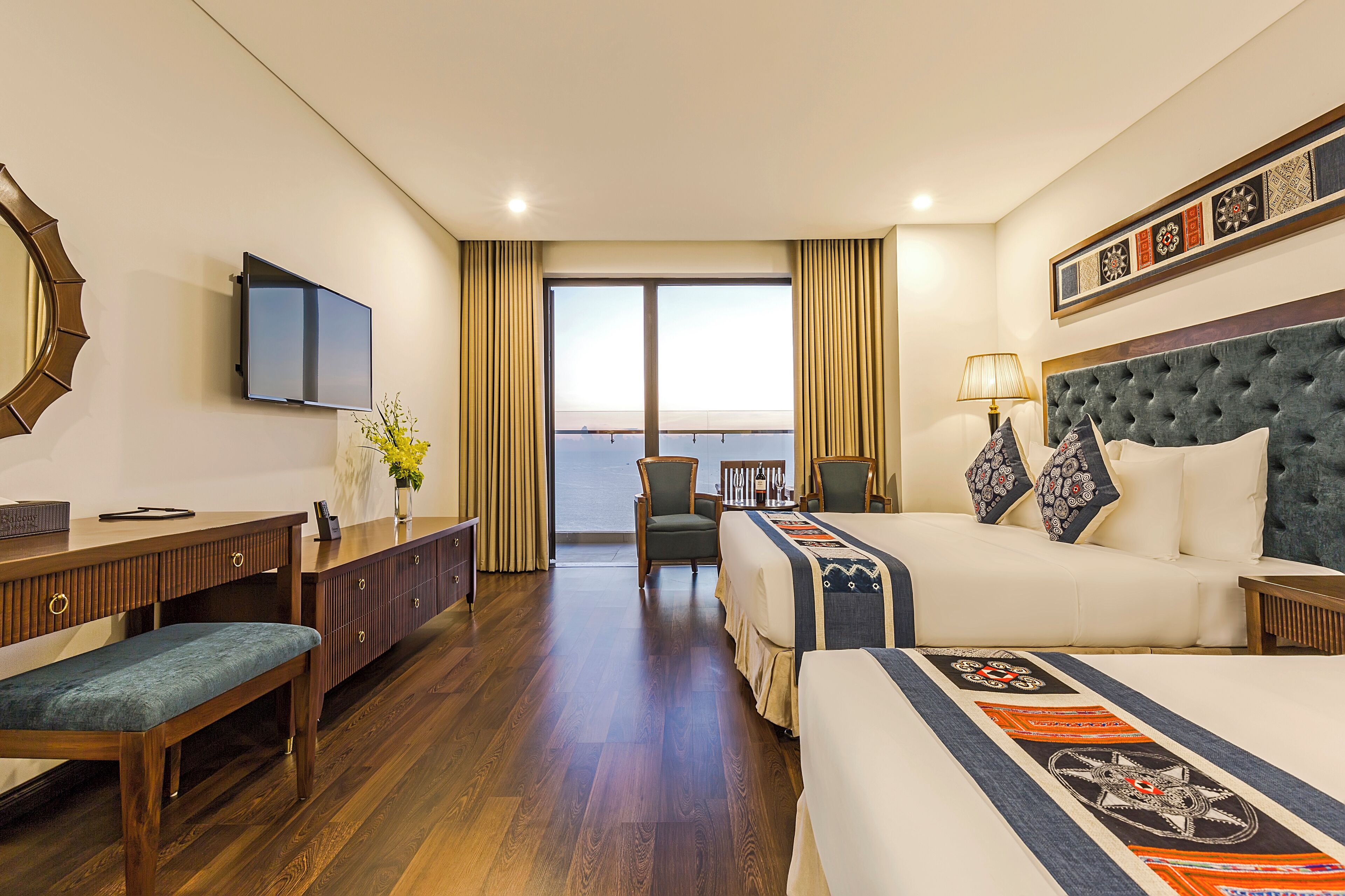 A hotel room with a bed, a desk, a chair, a TV, and a view of the sea.