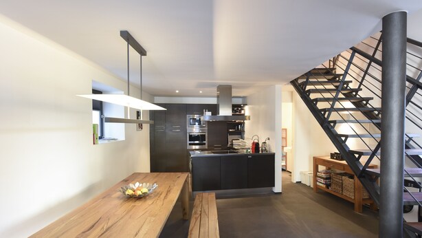Une cuisine moderne dotée d’un îlot central, d’une table à manger en bois et d’un escalier avec une rampe en métal.