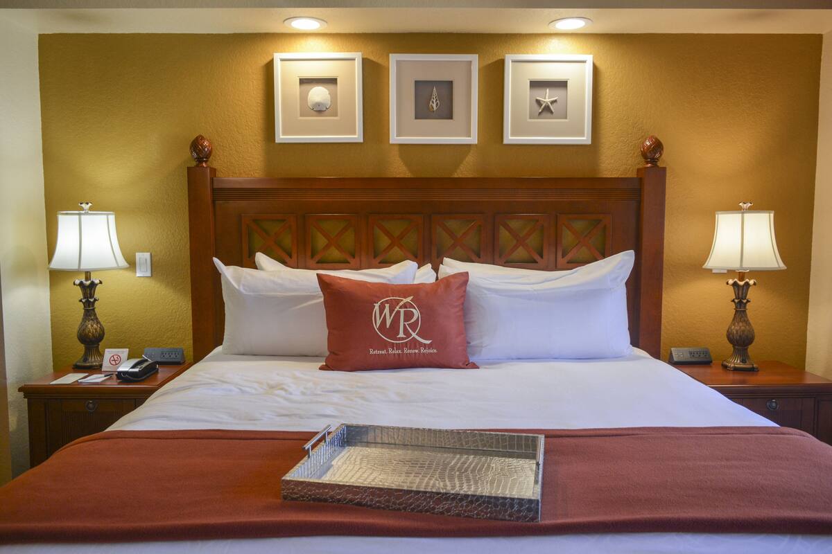 A hotel room with a large bed, two bedside tables, a tray, and framed pictures on the wall.