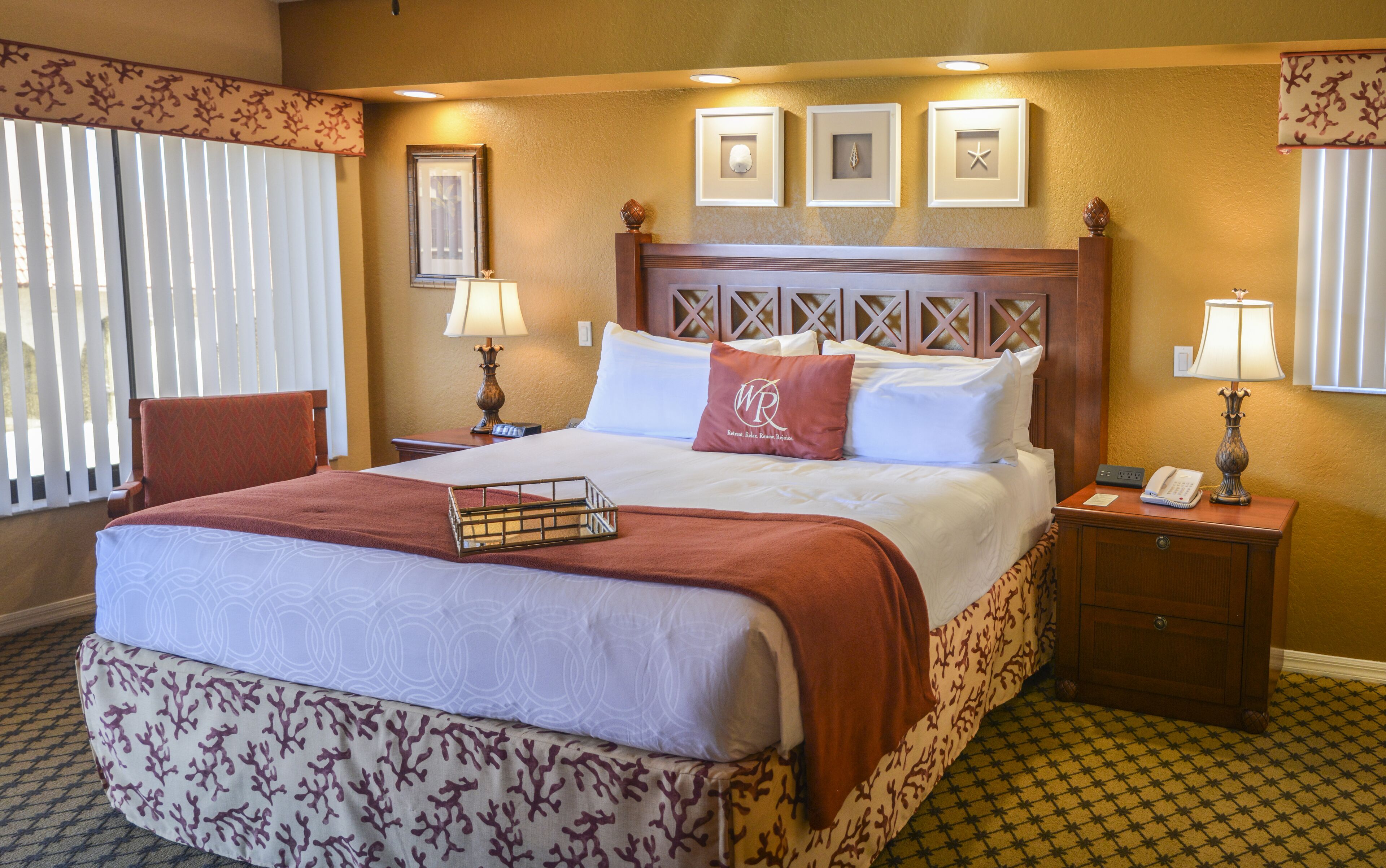 A hotel room with a large bed, a nightstand with a lamp, a chair, and a window with blinds.