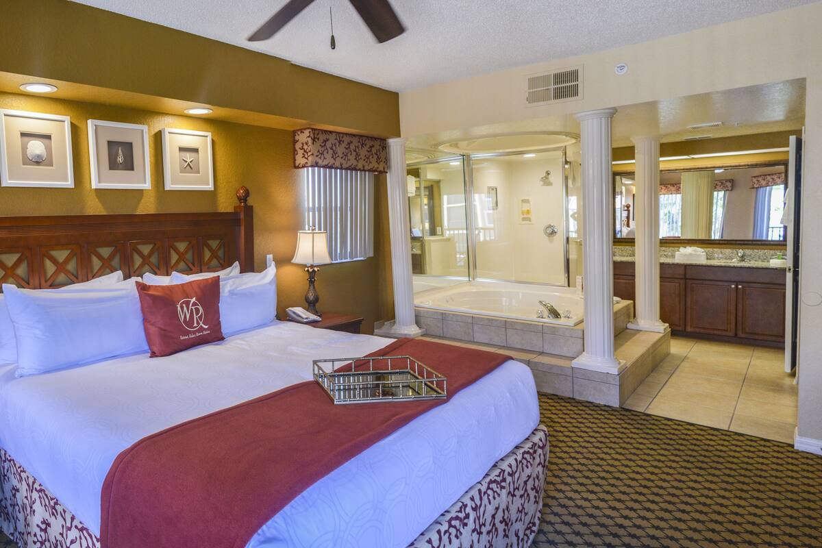A hotel room with a large bed, a bathroom with a bathtub, and a kitchen area.