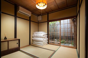 Una habitación japonesa tradicional con suelo de tatami, un montón de almohadas blancas, un armario de madera y un puertas correderas que dan a un jardín.