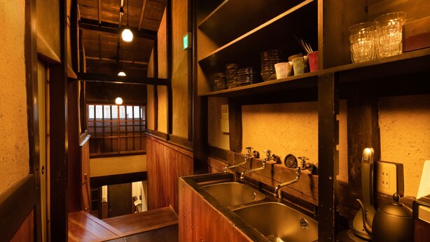 A narrow hallway with wooden walls and a metal sink. There are shelves above the sink with various items. - Kanade Fushimiinari (Kyoto)