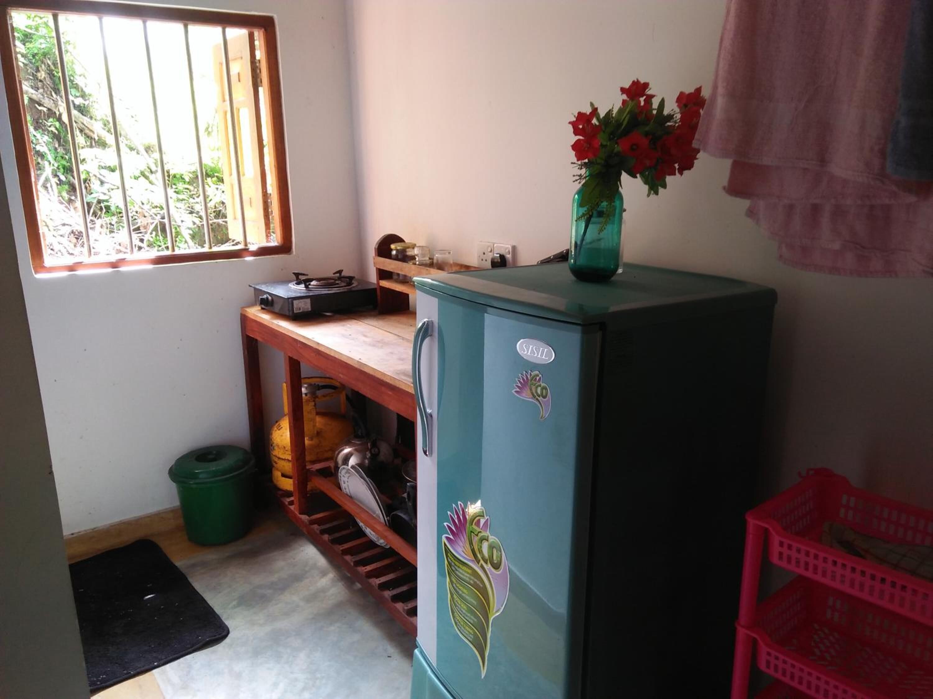 A compact kitchen with a refrigerator, a gas stove, a sink, and a window with bars.
