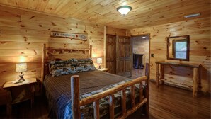 Un dormitorio tipo cabaña de troncos con una cama, mesitas de noche, un aparador y una chimenea.
