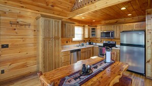 Cocina de estilo rústico con alacenas de madera, una isla central, electrodomésticos integrados y una escalera que sube a un nivel superior.