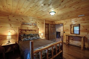 Un dormitorio tipo cabaña de troncos con una cama, mesitas de noche, un aparador y una chimenea.