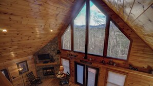 Una cabaña acogedora con chimenea de piedra, paredes de madera y ventanas amplias con vistas a la montaña.