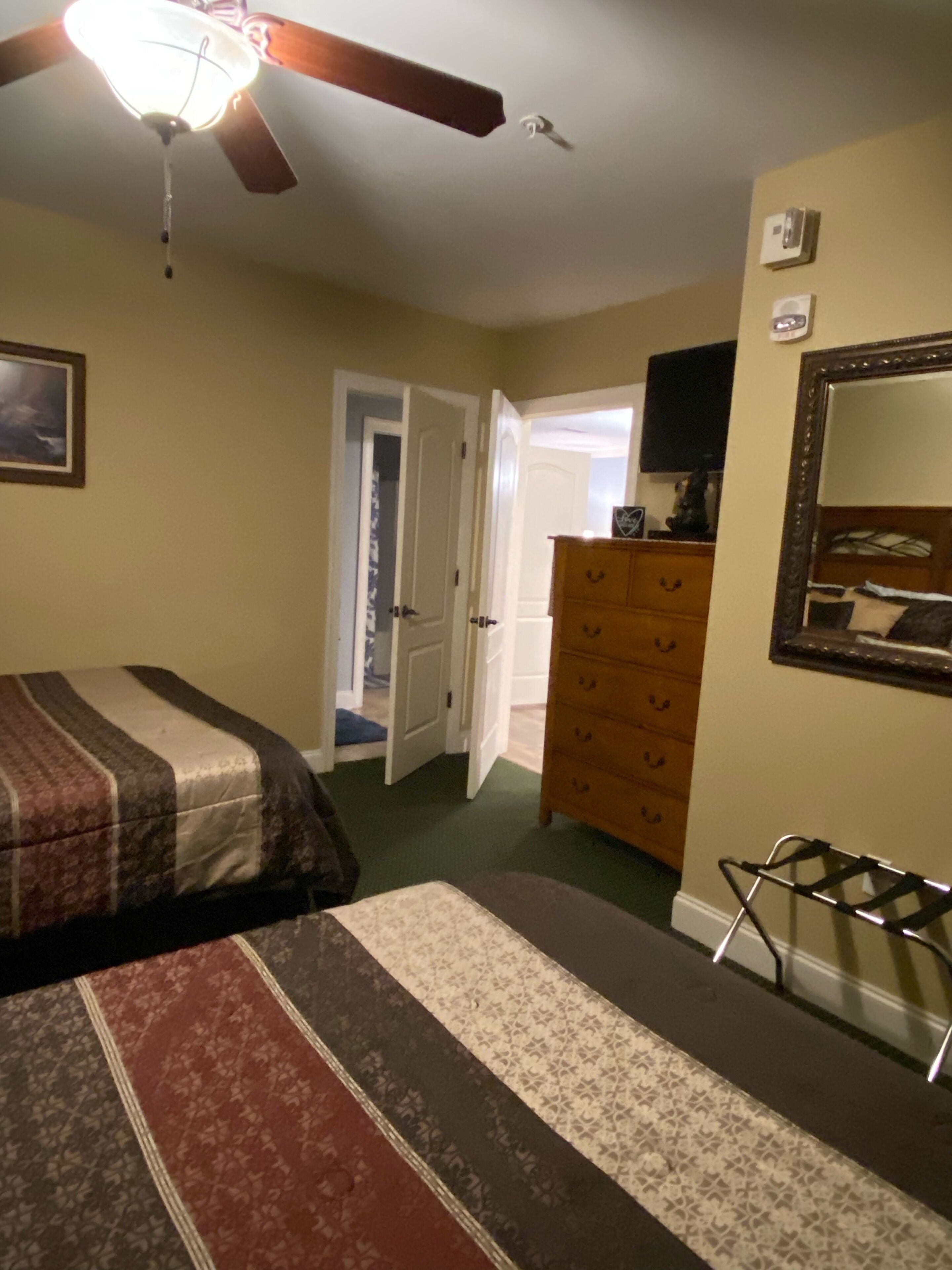 A bedroom with two beds, a dresser, a mirror, and a ceiling fan.
