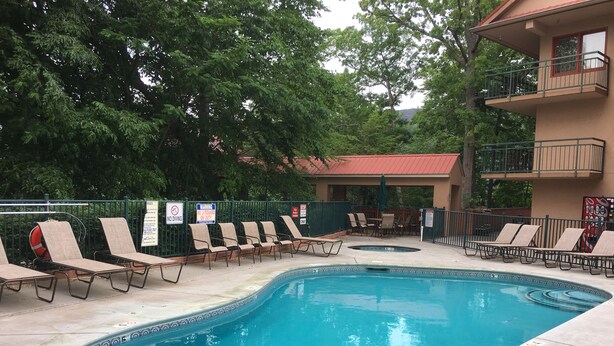 A swimming pool with lounge chairs and a covered seating area, surrounded by trees and a building with balconies. - Scenic Mountain View, Comforts of Home, Footsteps from Downtown Gatlinburg (Gatlinburg)