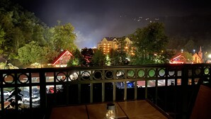 A night view from a balcony with a table and chairs, overlooking a town with illuminated buildings and trees. - Scenic Mountain View, Comforts of Home, Footsteps from Downtown Gatlinburg (Gatlinburg)