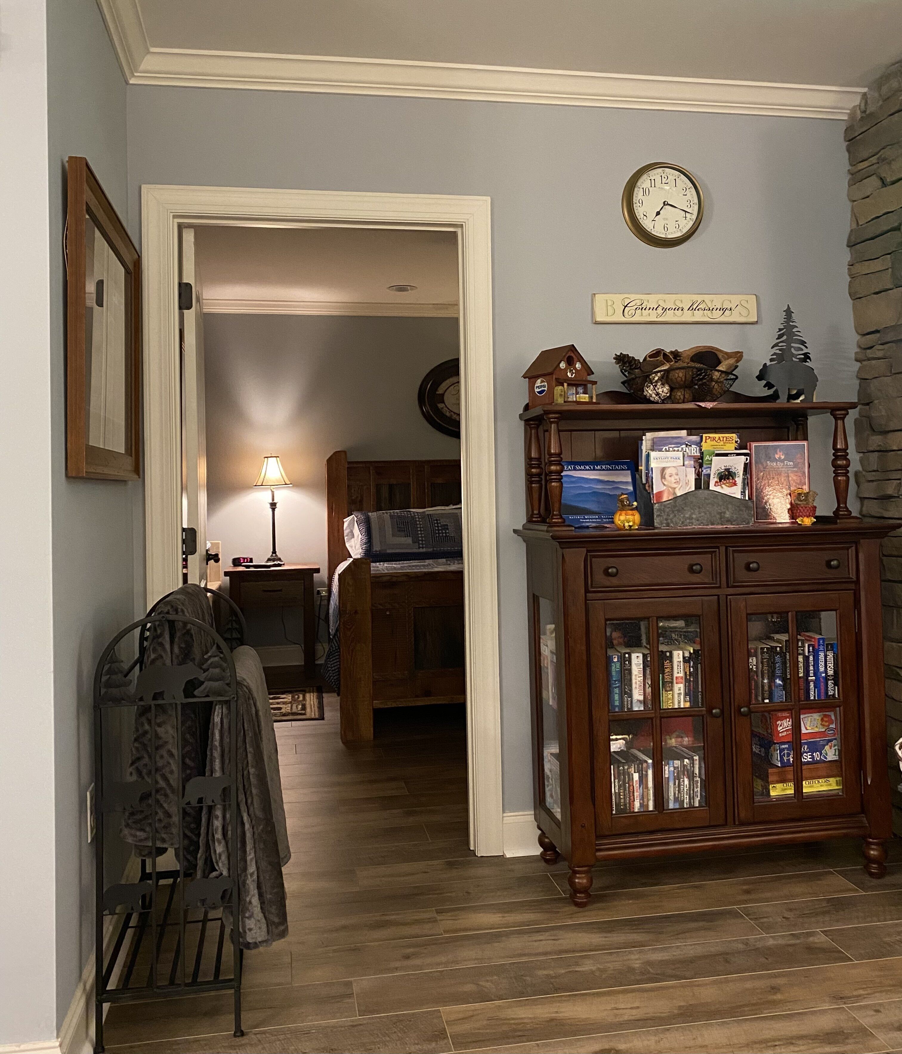 Ein Zimmer mit einem Holzkabinett, das mit Büchern und dekorativen Gegenständen gefüllt ist, einer Uhr an der Wand und einem Durchgang zu einem weiteren Raum.