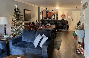 Uma sala de estar aconchegante com um sofá azul, uma árvore de Natal e um espaço de jantar com cadeiras de madeira e uma mesa.