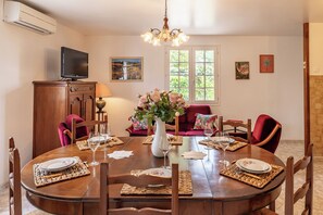 Comedor con una mesa redonda, sillas, un jarrón con flores, un televisor y obras de arte en las paredes.