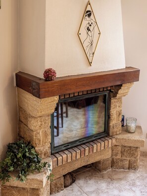 Una chimenea de piedra con repisa de madera, un adorno en la pared sobre ella, y una puerta de cristal que refleja la luz del interior.