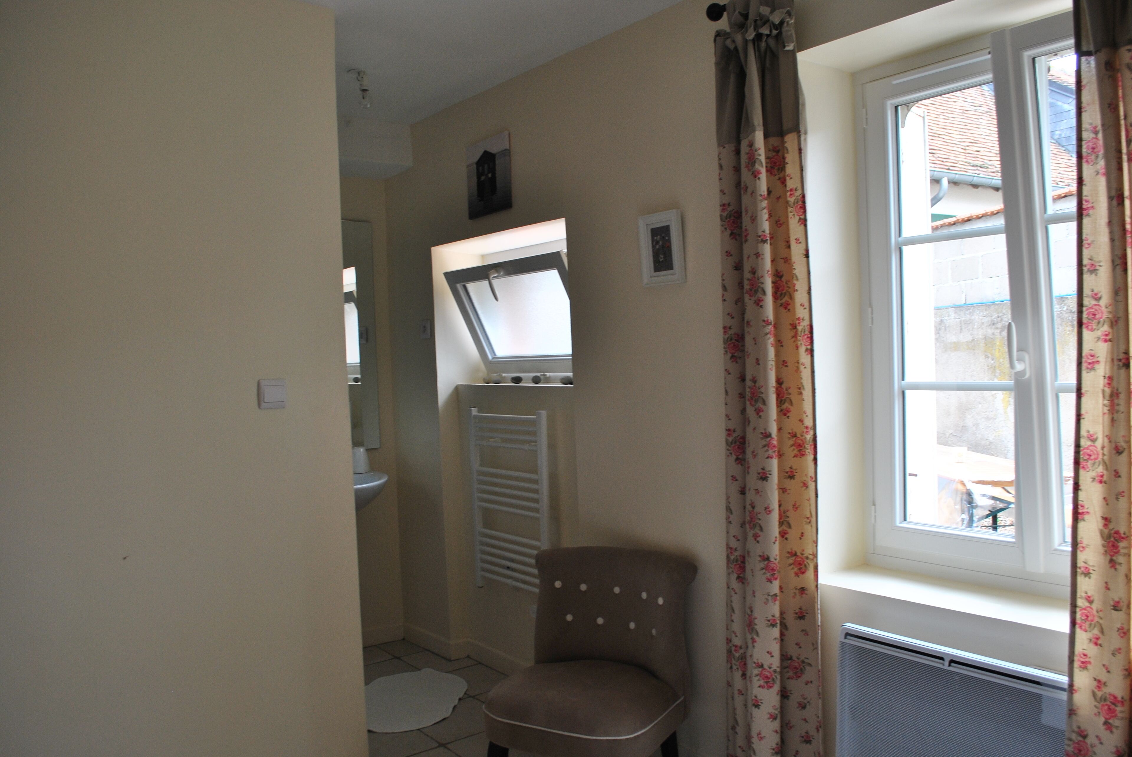 A bathroom with a toilet, a towel rack, a chair, and a window with curtains.